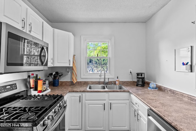 kitchen with appliances with stainless steel finishes, a sink, a textured ceiling, and white cabinets
