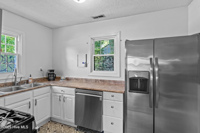 kitchen with stainless steel appliances, a sink, healthy amount of natural light, white cabinets, and a textured ceiling