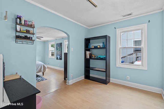 interior space featuring a textured ceiling, arched walkways, light wood finished floors, crown molding, and baseboards