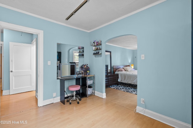 bedroom featuring crown molding, arched walkways, wood finished floors, baseboards, and a textured ceiling