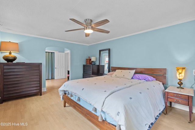 bedroom with wood finished floors, arched walkways, ornamental molding, a ceiling fan, and baseboards