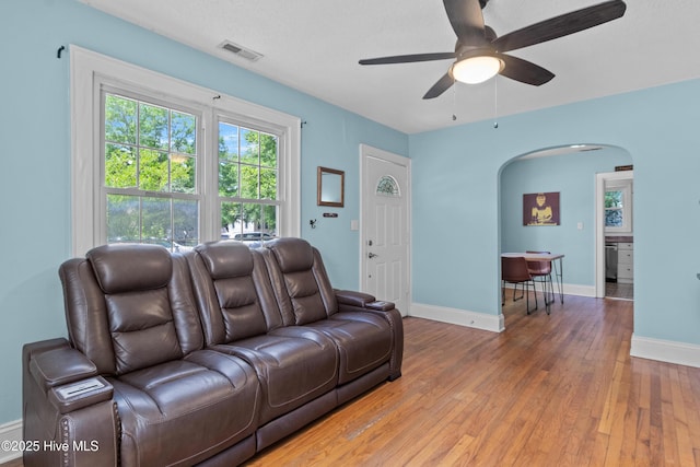 living area featuring arched walkways, ceiling fan, light wood finished floors, and baseboards