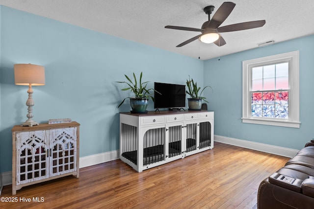 living area featuring wood finished floors, ceiling fan, baseboards, and a textured ceiling