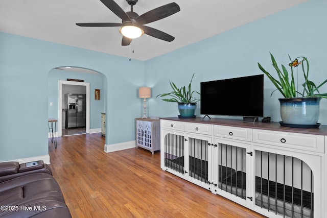 living area with arched walkways, ceiling fan, wood finished floors, and baseboards