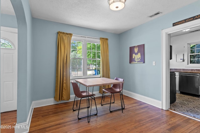 dining space featuring arched walkways, hardwood / wood-style flooring, a textured ceiling, and baseboards