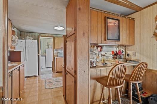 117 Arthur Rd, Beaufort, NC 28516 - kitchen featuring freestanding refrigerator, brown cabinetry, wood walls, a kitchen breakfast bar, and light countertops
