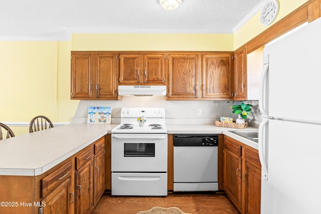 28 E First St Unit 4B, Ocean Isle Beach, NC 28469 - kitchen featuring white appliances, under cabinet range hood, a peninsula, light countertops, and brown cabinetry