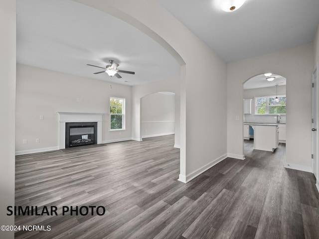 unfurnished living room featuring ceiling fan, dark wood-style floors, baseboards, and a glass covered fireplace