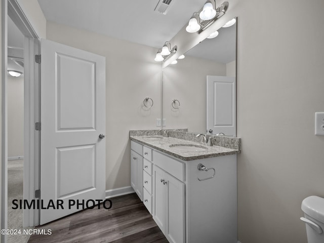 bathroom with double vanity, toilet, wood finished floors, and baseboards