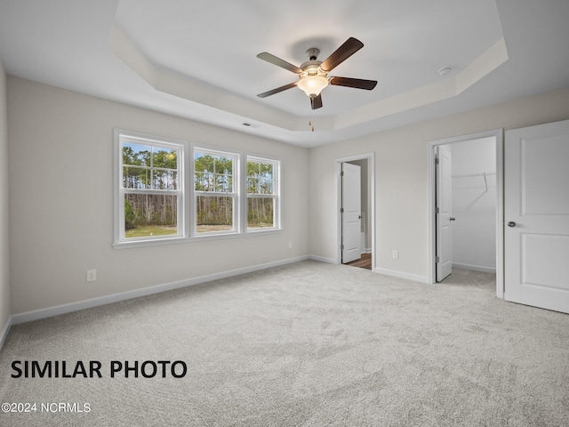unfurnished bedroom featuring a raised ceiling, carpet, baseboards, a ceiling fan, and a walk in closet