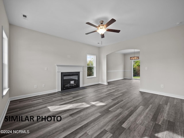 unfurnished living room with arched walkways, ceiling fan, dark wood-style flooring, baseboards, and a fireplace with flush hearth