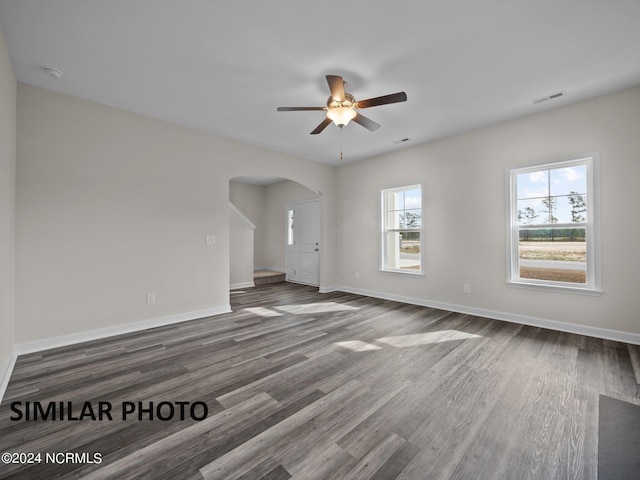 unfurnished room featuring arched walkways, ceiling fan, dark wood-type flooring, and baseboards