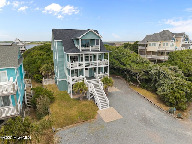 view of front of house with a balcony, stairway, driveway, and roof with shingles