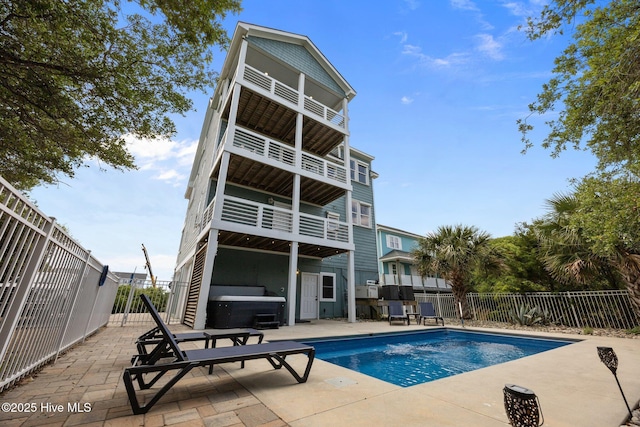 back of property with a hot tub, a patio, fence, and a balcony