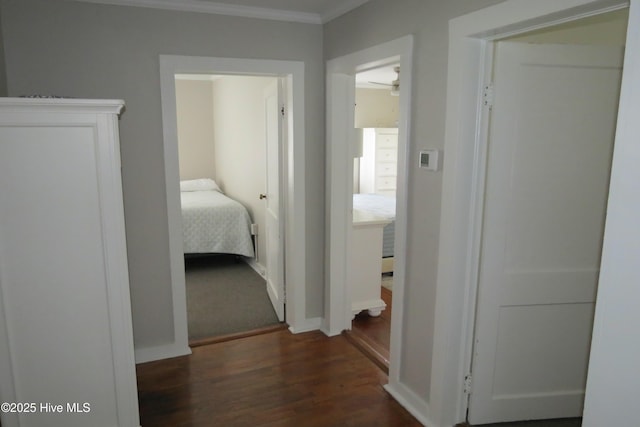 hall with dark wood-style flooring, crown molding, and baseboards