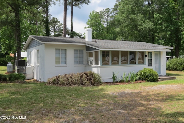 view of front facade featuring a chimney, a front lawn, central AC unit, and a shingled roof