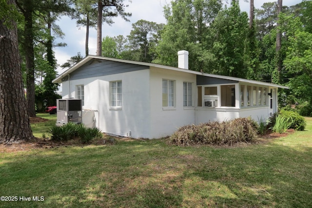 view of side of home with a chimney, a yard, central AC, stucco siding, and cooling unit