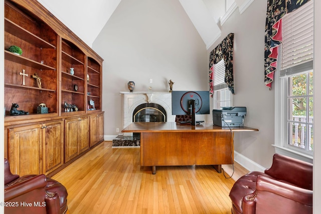 home office featuring light wood finished floors, healthy amount of natural light, a premium fireplace, and high vaulted ceiling
