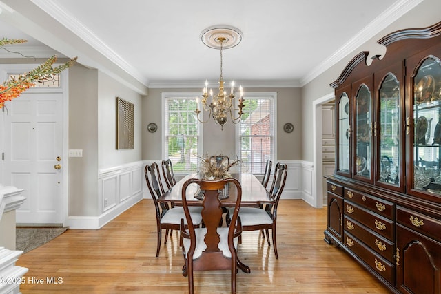 dining area with a chandelier, light wood-style floors, a wainscoted wall, ornamental molding, and a decorative wall