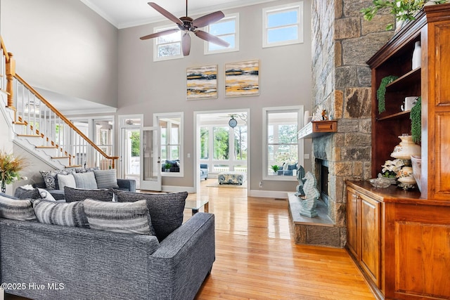 living area featuring stairway, a ceiling fan, light wood-style floors, ornamental molding, and a fireplace