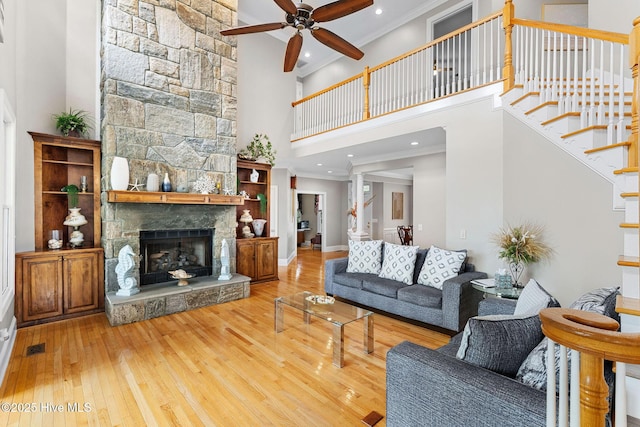 living room featuring a towering ceiling, wood-type flooring, ceiling fan, a fireplace, and crown molding