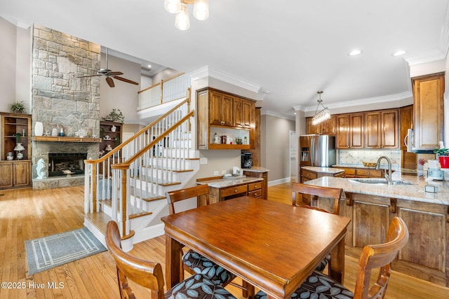 dining space with ceiling fan, light wood-style floors, crown molding, stairs, and a stone fireplace