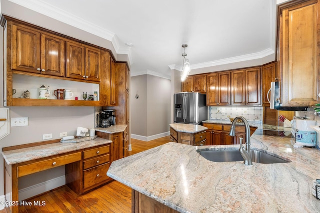 kitchen featuring appliances with stainless steel finishes, a sink, baseboards, brown cabinets, and light stone counters