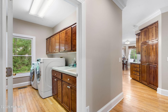 washroom with cabinet space, light wood-type flooring, healthy amount of natural light, independent washer and dryer, and crown molding