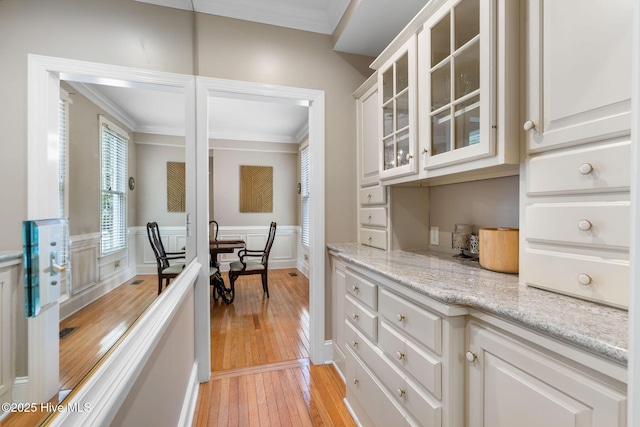 bar featuring crown molding, light wood finished floors, a wainscoted wall, and a decorative wall