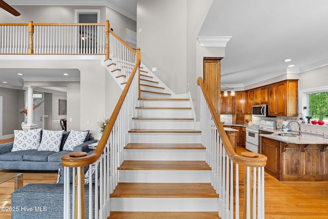 stairs with wood finished floors, crown molding, ornate columns, and recessed lighting