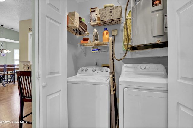 washroom featuring washing machine and clothes dryer, water heater, wood finished floors, a textured ceiling, and a chandelier