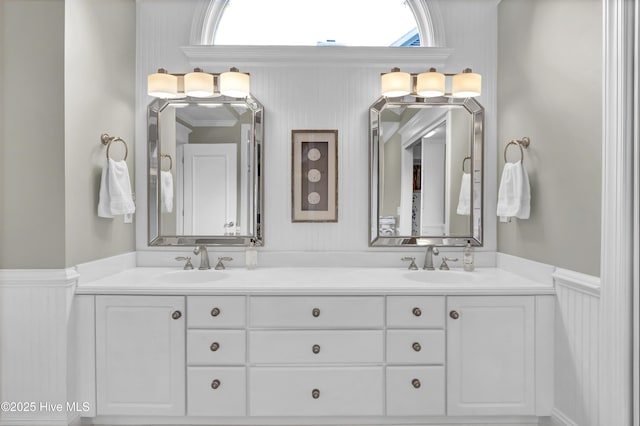 bathroom with wainscoting, double vanity, and a decorative wall