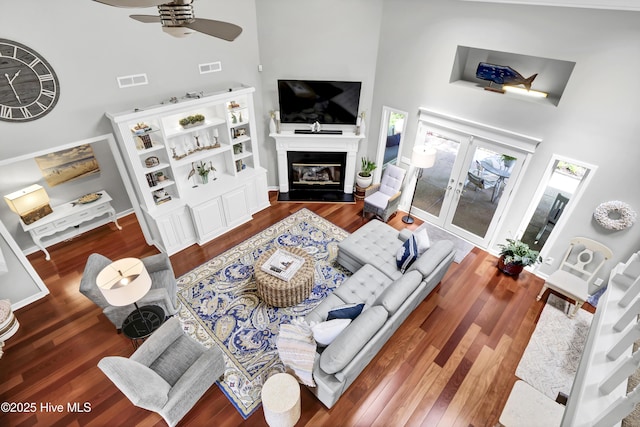 living area with high vaulted ceiling, ceiling fan, wood finished floors, a glass covered fireplace, and french doors