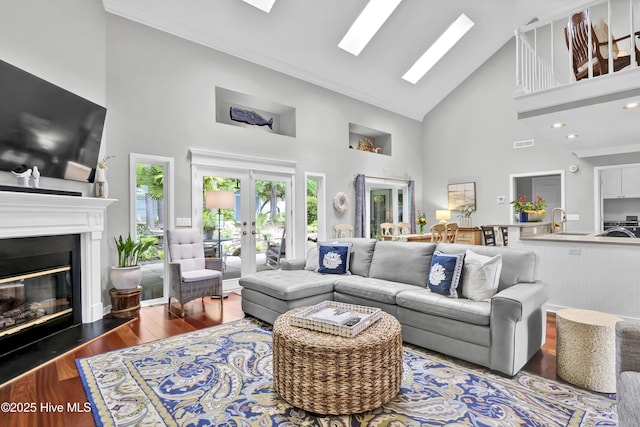 living area with high vaulted ceiling, wood finished floors, a glass covered fireplace, and french doors