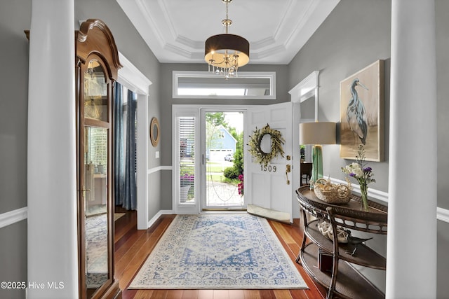 entrance foyer featuring a raised ceiling, wood-type flooring, ornamental molding, and a chandelier