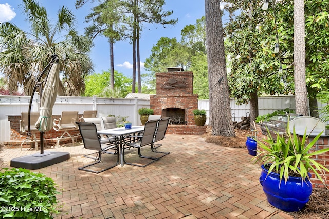 view of patio / terrace with an outdoor brick fireplace, outdoor dining space, and fence