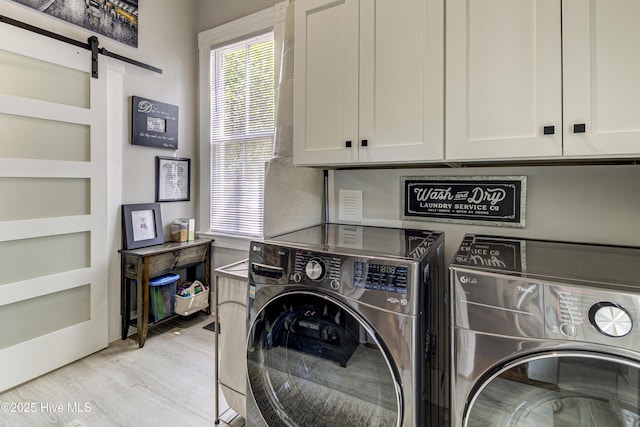 clothes washing area with cabinet space, washer and dryer, light wood-style floors, a barn door, and healthy amount of natural light