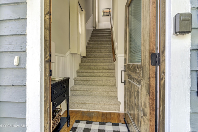 staircase featuring wood finished floors and a wainscoted wall