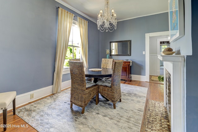 dining space featuring a chandelier, crown molding, wood finished floors, baseboards, and a fireplace with flush hearth
