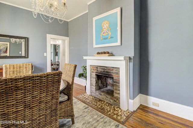 living area featuring ornamental molding, a chandelier, a fireplace, wood finished floors, and baseboards