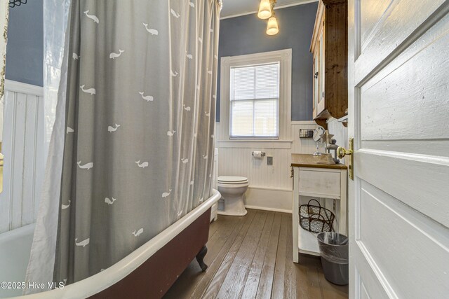 bathroom with a wainscoted wall, toilet, hardwood / wood-style floors, shower / bath combo with shower curtain, and ornamental molding