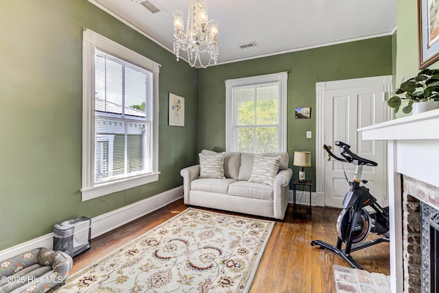 living room featuring crown molding, a fireplace, a chandelier, wood finished floors, and baseboards