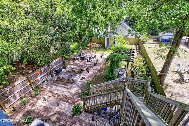fenced backyard with a garden, a wooden deck, stairway, and an outdoor fire pit
