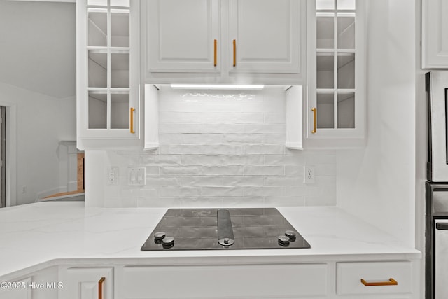 1103 Groppo Cv, Wilmington, NC 28412 - kitchen with black electric cooktop, glass insert cabinets, white cabinets, decorative backsplash, and light stone counters
