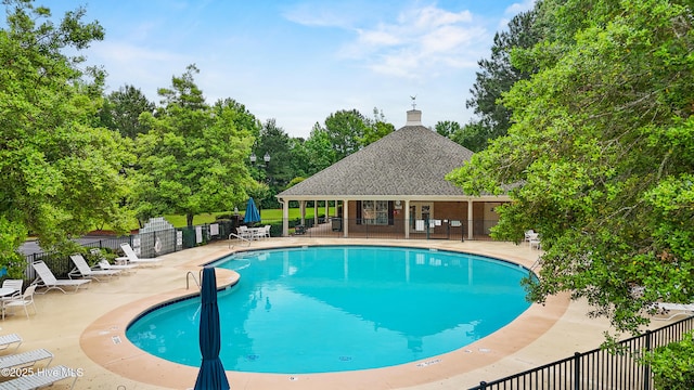 community pool with fence, a patio area, and view of wooded area
