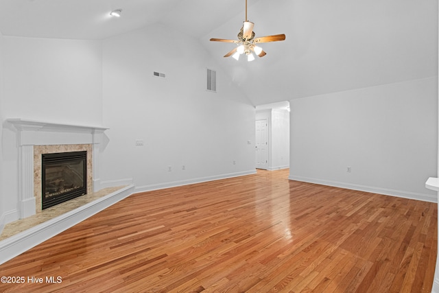 unfurnished living room with ceiling fan, high vaulted ceiling, light wood-style floors, a high end fireplace, and baseboards