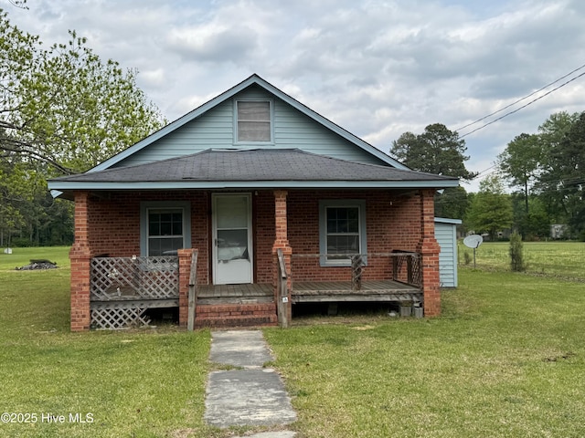 view of front facade with a porch, a front yard, roof with shingles, and brick siding