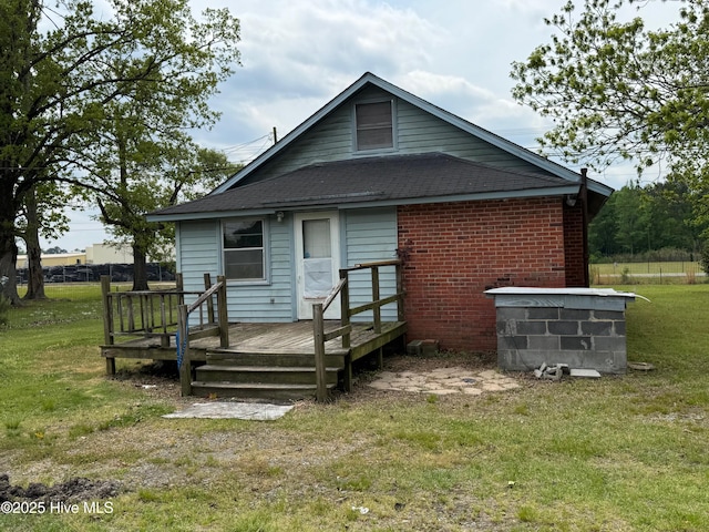 rear view of house featuring a deck, a yard, a shingled roof, and brick siding