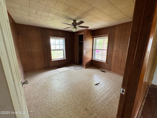 spare room featuring plenty of natural light, wooden walls, ceiling fan, and baseboards