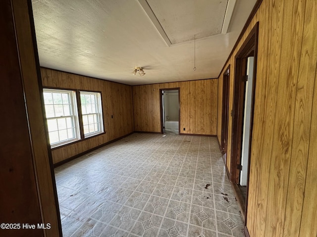 unfurnished room with attic access, baseboards, and wooden walls